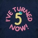 Close-up of the I've Turned 5 Now! birthday embroidery on a navy kids tshirt showing the quilted texture of the number